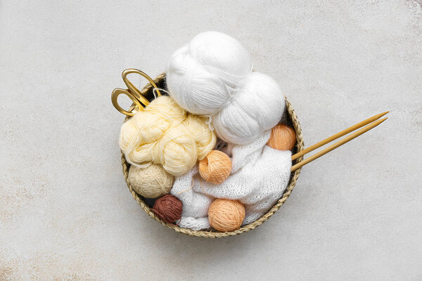 Basket with yarn balls, knitting needles and scissors on grey table