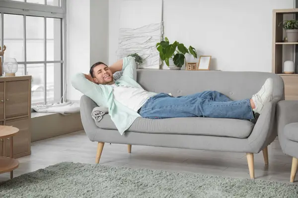 stock image Young man lying on grey sofa at home