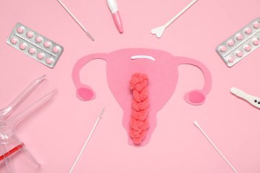 Pembe arka planda jinekolojik spekulumlu kağıt rahim, haplar ve pap smear test araçları