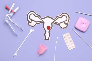 Jinekolojik spekulumlu kağıt rahim, haplar, regl kupası ve mor arka planda pap smear testi aletleri.