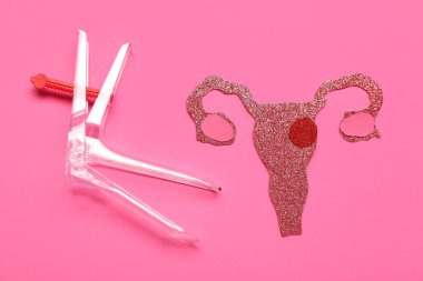 Pembe arka planda jinekolojik spekulumu olan kağıt rahim.