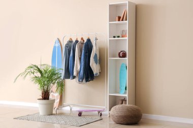 Renkli duvarın yanında şık kadın kıyafetleri, ev bitkisi ve spor malzemeleri rafı.