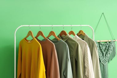 Rack with stylish female clothes near green wall in room, closeup clipart