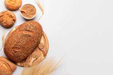 Beyaz arka planda bir somun taze ekmek, çörek, kase, kaşık ve buğday taneleri.