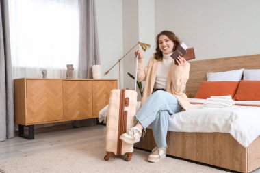 Otel odasında bavulu ve pasaportu olan bir kadın turist oturuyor.