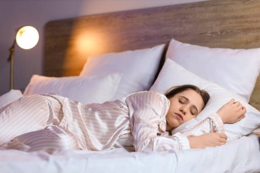 Pijamalı genç kadın geceleri yatakta uyuyor.