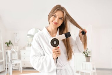 Güzel bir kadın banyoda saçlarını yuvarlak fırçayla kurutuyor.