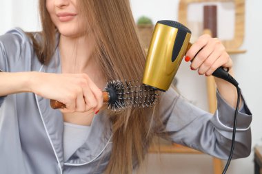 Saçını banyoda kurutan yuvarlak fırçalı genç bir kadın.