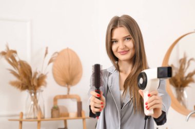 Banyoda saç kurutma makinesi ve yuvarlak fırçası olan genç bir kadın.