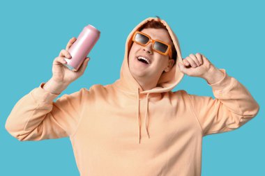 Mavi arka planda bir kutu sodayla güneş gözlüklü genç adam.