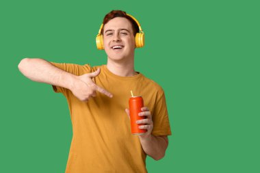 Kulaklıklı genç adam yeşil arka plandaki soda kutusunu işaret ediyor.