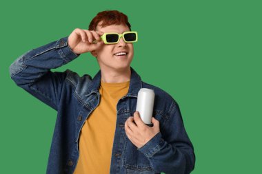 Yeşil arka planda bir kutu sodayla güneş gözlüklü genç adam.