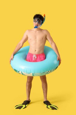 Sarı arka planda şnorkel maskeli ve şişme yüzüklü yakışıklı genç adam.