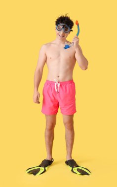 Sarı arka planda şnorkel maskesi ve paletleri olan yakışıklı genç adam.