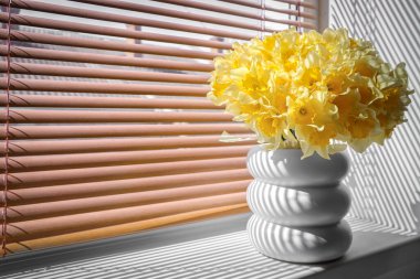 Odadaki pencere eşiğinde nergisler olan vazo.