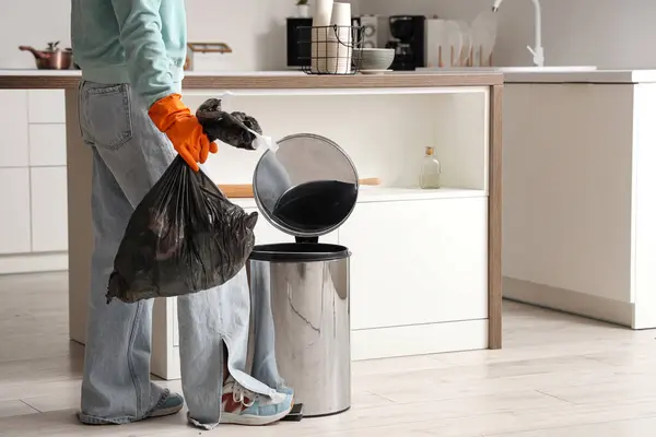 Woman taking full garbage bag from trash bin in light kitchen