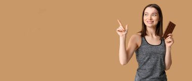 Çikolatalı genç kadın bej arka planda mesaj için yeri olan bir şeyi işaret ediyor.