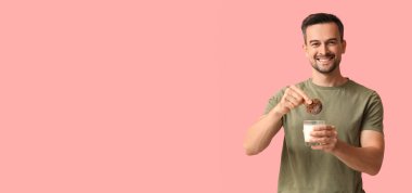 Lezzetli kurabiyesi ve pembe arka planda bir bardak sütü olan yakışıklı bir adam.