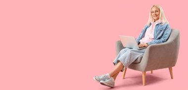 Dizüstü bilgisayarı pembe arka planda, metin için yeri olan olgun bir kadın programcı.