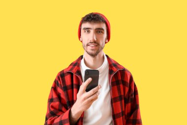 Sarı arka planda cep telefonu kullanan yakışıklı genç adam.