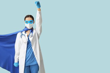 Süper kahraman kostümlü güzel bayan doktor ve mavi arka planda tıbbi maske.