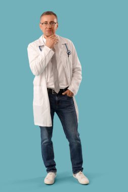 Mavi arka planda tıp önlüğü giymiş olgun bir doktor.
