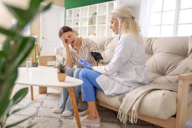 Kadın doktor, evdeki hastanın tansiyonunu ölçüyor.