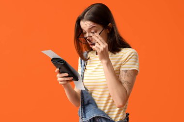 Turuncu arka planda cüzdanı ve fişi olan şok olmuş genç bir kadın. Fiyat artışı kavramı