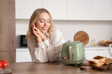 Mutfakta modern tost makinesi olan güzel, mutlu bir kadın.