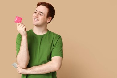 Bej arka planda prezervatifli genç bir adam. Güvenli seks konsepti