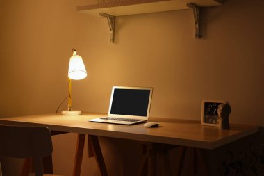 Modern dizüstü bilgisayarı ve gece lambasıyla rahat bir iş yeri.