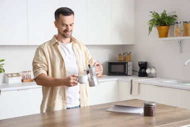 Yakışıklı adam gayzer kahve makinesinden modern mutfakta fincana espresso dolduruyor.