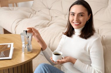 Oturma odasında gayzer kahve makinesi ve bir fincan espresso ile güzel genç bir kadın, yakın plan.