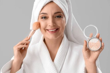 Bornozlu olgun bir kadın hafif arka planda duş aldıktan sonra fosforlu kalem kullanıyor.