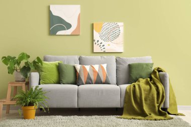 Yeşil duvarın yanındaki yastıklı, resimli ve çiçekli şık gri kanepe.