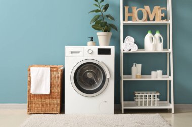 Çamaşır sepeti, çamaşır makinesi ve raf ünitesi olan odanın içi.