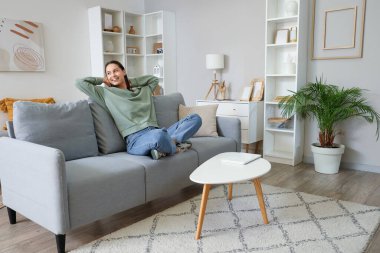 Oturma odasındaki gri kanepede oturan genç kadın.