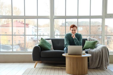 Genç adam oturma odasında dizüstü bilgisayar kullanıyor.