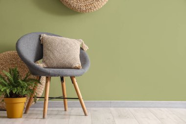 Oturma odasının içinde yeşil duvarın yanında koltuk, yastık ve çiçek var.