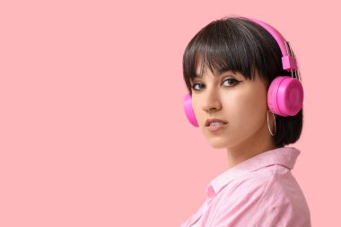 Pembe arka planda burun piercingli, kulaklıklı şık genç bir kadın.