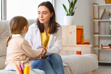 Ofiste el ele tutuşan küçük bir kız ile kadın psikolog.