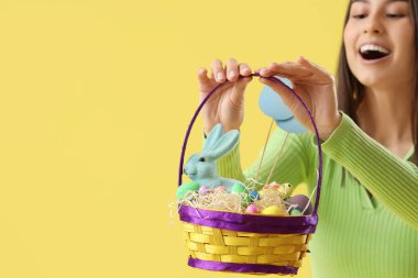 Sarı arka planda Paskalya yumurtası sepeti olan genç bir kadın, yakın plan.