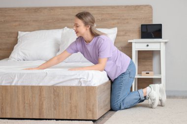 Modern yatak odasında yatak yapan güzel genç bir kadın.