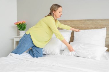 Modern yatak odasında yastık koyan güzel bir genç kadın.