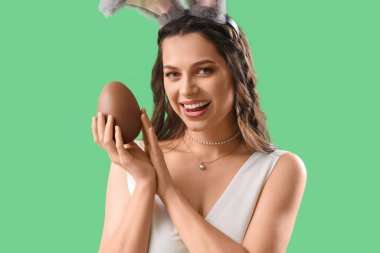 Yeşil arka planda çikolatalı Paskalya yumurtası olan tavşan kulaklı güzel bir kadın.