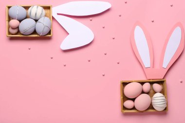 Renkli Paskalya yumurtaları ve pembe arka planda kağıt tavşan kulakları olan etiket kutuları.