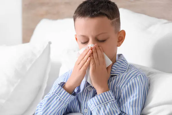 Ill little boy with tissue sneezing in bedroom, closeup