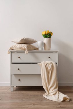 Yatak odasındaki ışık duvarının yanındaki tuvalette lale ve yastıklı vazolar.