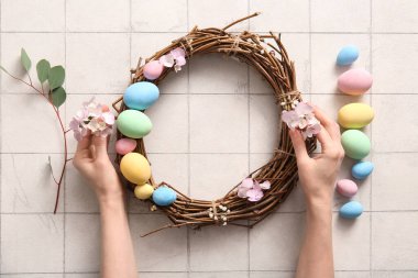 Beyaz fayansla boyanmış yumurta ve çiçeklerle Paskalya çelengi yapan kadın.
