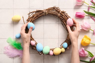 Beyaz fayanslı yumurta, tüy ve lale çiçeklerinden Paskalya çelengi yapan kadın.